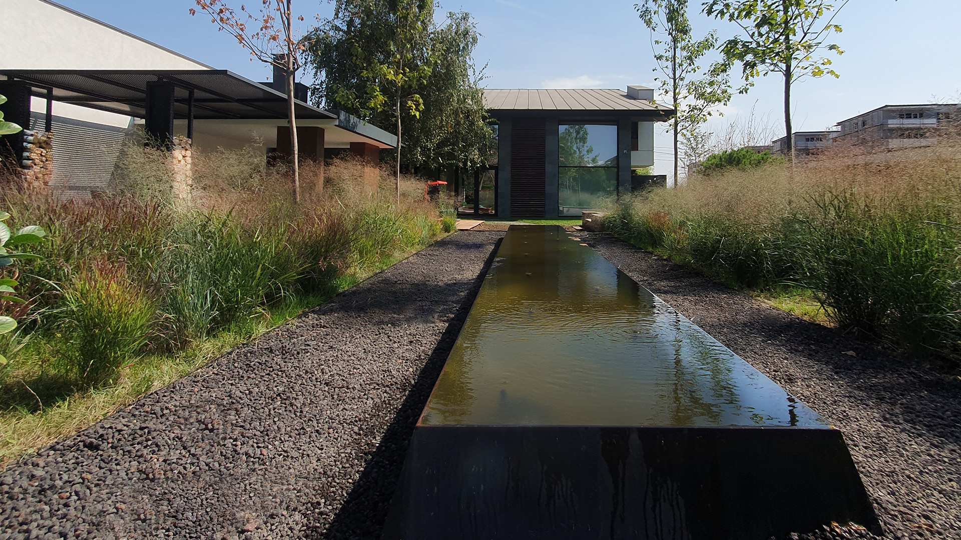 Ax de perspectivă cu bazin metalic cu apă reflectantă și alee cu pietriș printre ierburi ornamentale