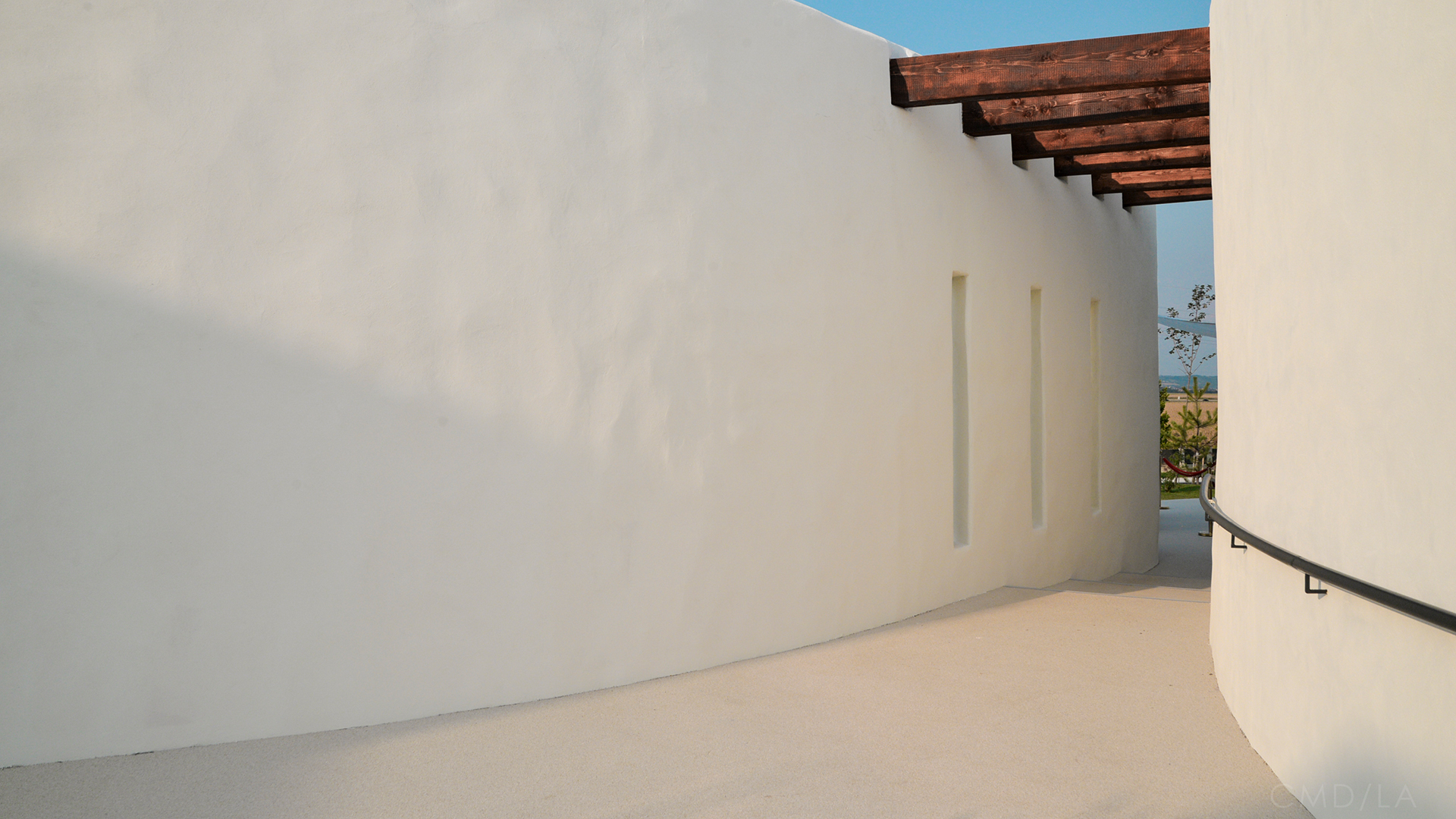 Pasaj curbat între pavilioanele Ramatuelle, cu pereți albi și pergolă de lemn – design inspirat mediteranean.